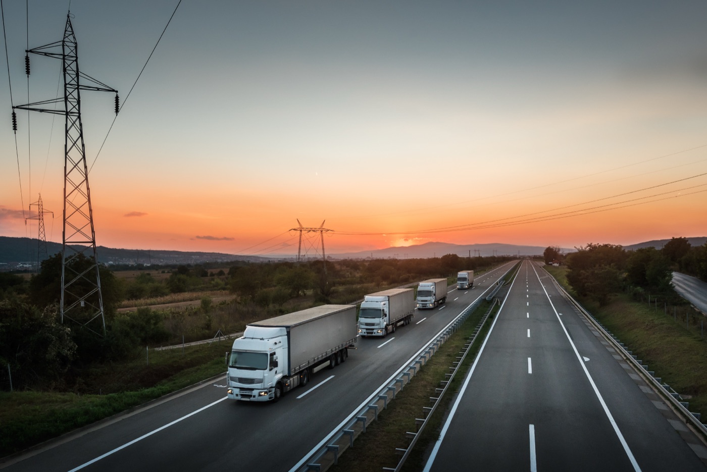 Camiões em coluna numa autoestrada ao pôr do sol